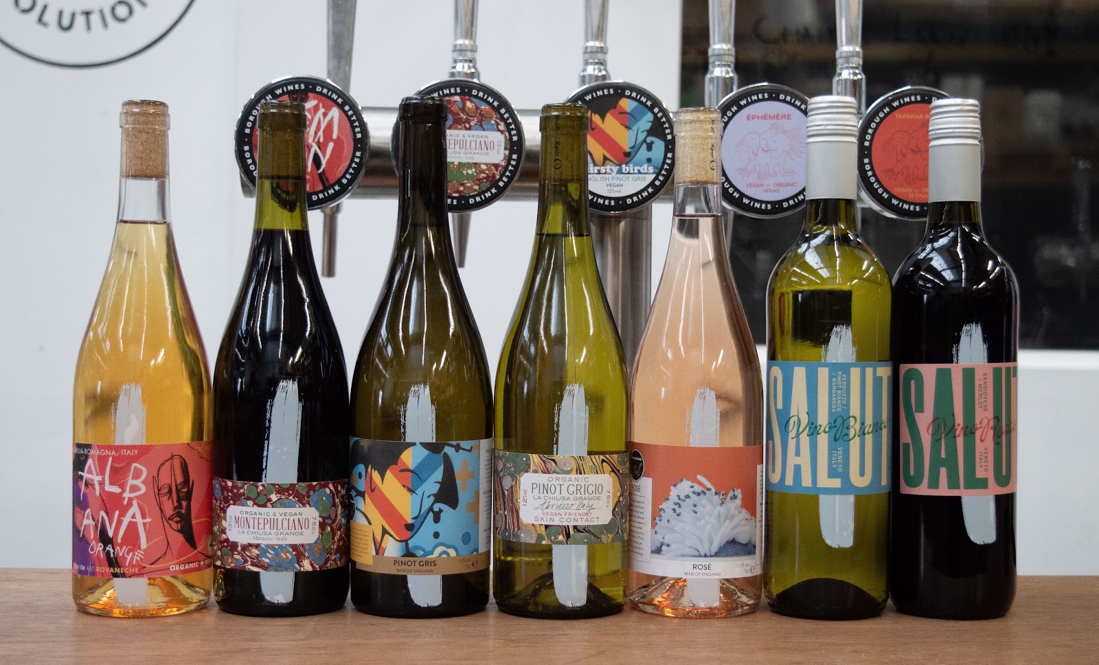 A line of Borough Wines bottles in front of the taps, from Albana Orange and Montepulciano to English Pinot Gris, rosé and Salut, each keg badged Borough Wines, Drink Better.